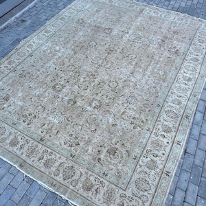 K&ouml;nnte beinhalten: Ein Vintage-Teppich mit beigefarbenem Hintergrund und einem floralen Muster in Braun- und Gr&uuml;nt&ouml;nen. Der Teppich hat einen Rand mit einem sich wiederholenden Muster.