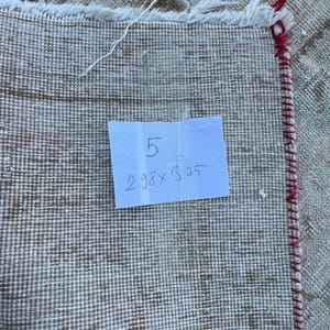 K&ouml;nnte beinhalten: Nahaufnahme eines wei&szlig;en Teppichs mit rotem Rand. Ein handschriftlicher Zettel auf einem wei&szlig;en Blatt Papier lautet "5 2.98 x 3.25".