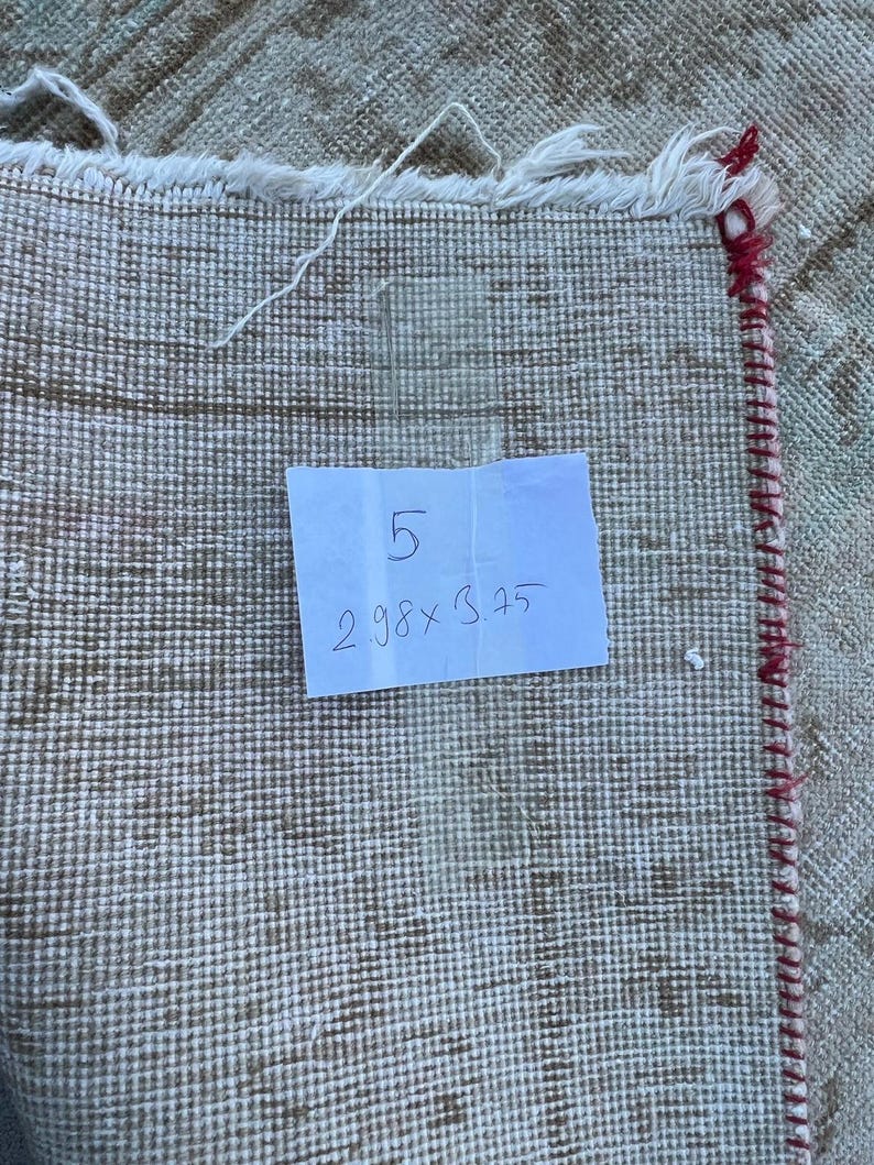 K&ouml;nnte beinhalten: Nahaufnahme eines wei&szlig;en Teppichs mit rotem Rand. Ein handschriftlicher Zettel auf einem wei&szlig;en Blatt Papier lautet "5 2.98 x 3.25".
