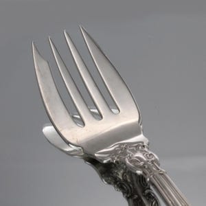 May include: Close-up of a silver fork with a decorative handle. The fork has five tines and a slightly ornate design.