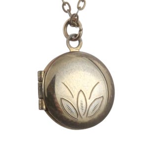 May include: A gold locket necklace with a floral design on the front. The locket is round and has a hinged lid.