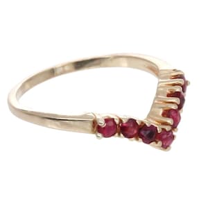 May include: A gold band ring with a V-shaped row of red gemstones.
