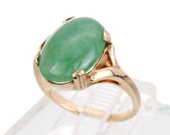 May include: A gold ring with a large oval green jade stone. The ring has a delicate, ornate design.