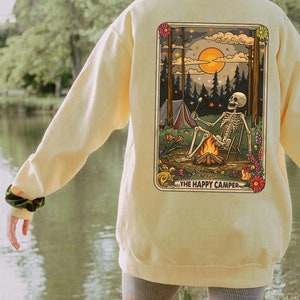 May include: A yellow sweatshirt with a graphic print of a skeleton camping in the woods. The graphic includes the text "The Happy Camper".