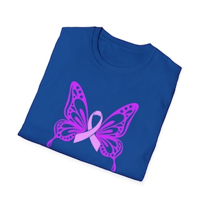 Op de afbeelding: Een koningsblauw t-shirt met een roze vlinderontwerp en een roze lint in het midden. De vlinder heeft gedetailleerde vleugelpatronen. Het t-shirt is opgevouwen en toont het ontwerp.