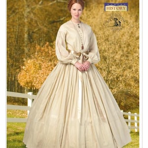 May include: A woman in a cream-colored historical dress with vertical stripes, long sleeves, and a ribbon belt. The dress is from a Butterick pattern, B5831, and is part of the Making History collection. The background is a blurred autumn scene.