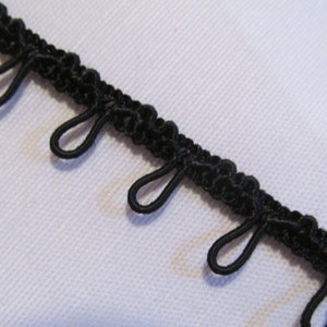 May include: Black elastic trim with loops. The trim is made of a soft, flexible material and has a series of evenly spaced loops along one edge.