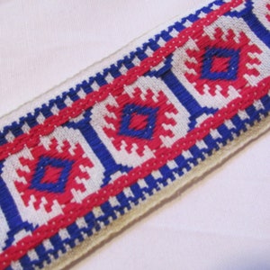May include: White fabric with a red, blue, and white woven trim. The trim has a geometric pattern.