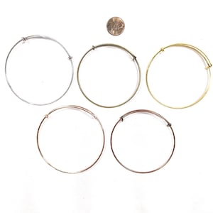 May include: Five thin, adjustable wire bangles in silver, gold, antique brass, rose gold, and copper tones. Each bracelet features a sliding mechanism for sizing. A US penny is placed above the bangles for scale, measuring 0.75 inches in diameter.