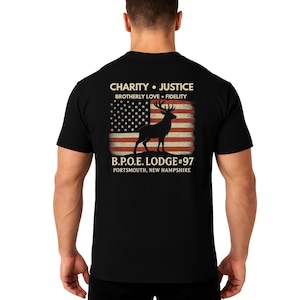 May include: Black t-shirt featuring a graphic of a deer silhouette in front of a distressed American flag. The shirt includes text that reads "CHARITY • JUSTICE, BROTHERLY LOVE • FIDELITY" and "B.P.O.E. LODGE #97, PORTSMOUTH, NEW HAMPSHIRE."
