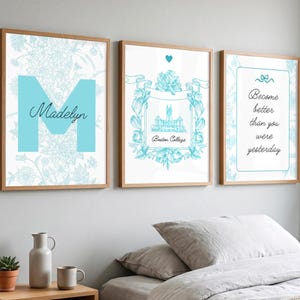 Op de afbeelding: Drie ingelijste wandkunstprints met lichtblauwe en witte bloemmotieven. De eerste toont een grote letter M met de naam Madelyn. De tweede toont een illustratie van Boston College. De derde toont de tekst Become better than you were yesterday.