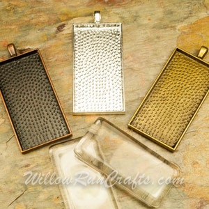 May include: Four rectangular pendant trays with a textured surface. The trays are in silver, gold, black, and clear glass.