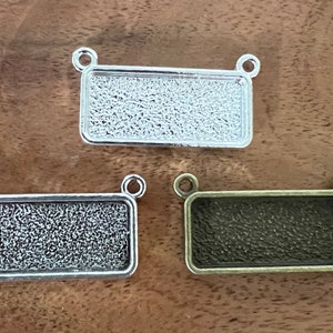 Peut inclure: Trois plateaux rectangulaires en métal pour pendentif avec une surface texturée. Les plateaux sont argentés, argentés antiques et bronze.