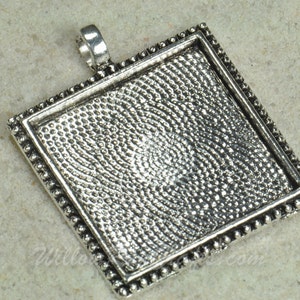 May include: Silver-toned square pendant with a textured surface and a beaded border. The pendant has a loop at the top for attaching a chain.
