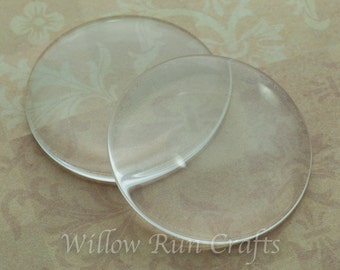 May include: Two clear glass circles, one slightly larger than the other, are shown on a light brown patterned surface. The circles are smooth and translucent.