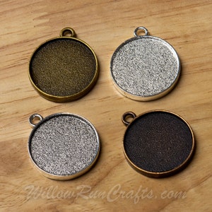 May include: Four round metal pendant trays in different finishes: antique brass, silver, black, and antique copper. Each tray has a smooth, slightly textured surface and a loop at the top for hanging.