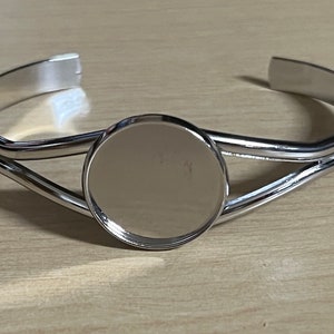 May include: Silver bangle bracelet with a round, blank, silver-toned metal charm in the centre.