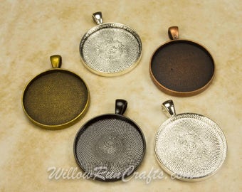 May include: Five round metal pendant trays with different finishes: silver, antique brass, copper, black, and silver. Each tray has a raised edge and a loop for hanging.