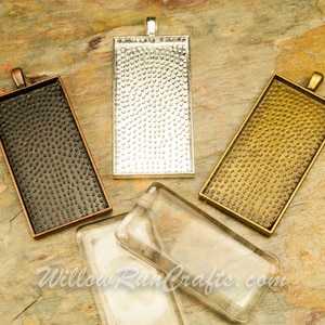 May include: Four rectangular pendant trays with a textured surface. The trays are in silver, gold, black, and clear glass.