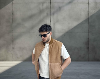 May include: A brown fleece vest with a zipper closure. The vest has a contrasting brown fabric panel on the bottom. The person wearing the vest is also wearing a white t-shirt and dark blue jeans.