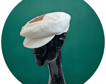 May include: A white linen newsboy cap with a colorful graphic design on the front.