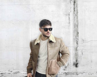 May include: A brown leather jacket with a shearling collar and a zipper closure. The jacket has a patch pocket on the left side and a zippered pocket on the right side.