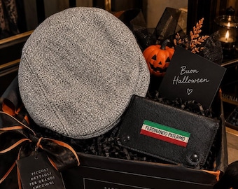 May include: A grey tweed flat cap and a black leather wallet featuring a rectangular patch with the Italian flag colors and the text FERDINANDO PATERMO, presented in a gift box with a small orange pumpkin and a card reading Buon Halloween.