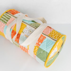 May include: A patchwork fabric duffel bag with a cream-colored zipper and straps. The bag is made of various fabrics with floral and geometric patterns in shades of yellow, orange, green, blue, and pink. The bag has a label that reads "Sequoia National Park".