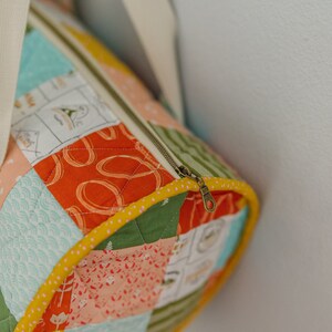 May include: A patchwork fabric duffel bag with a yellow trim and a brass zipper pull. The bag is made of different patterned fabrics in shades of blue, green, orange, and pink.