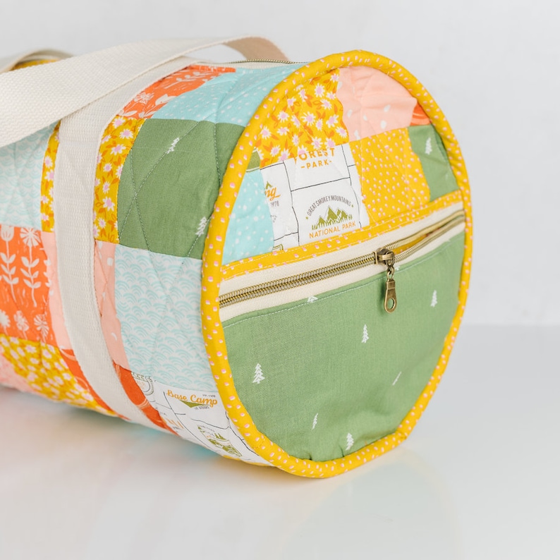 May include: A yellow and green quilted duffel bag with a zippered pocket and a white strap. The bag has a patchwork design with various patterns, including flowers, trees, and a map. The text "Great Smoky Mountains National Park" is printed on the bag.