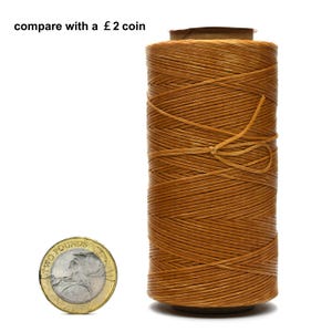 May include: A spool of brown waxed thread for leather crafting, next to a two pound coin for size comparison.  "compare with a £2 coin" is written above the spool.