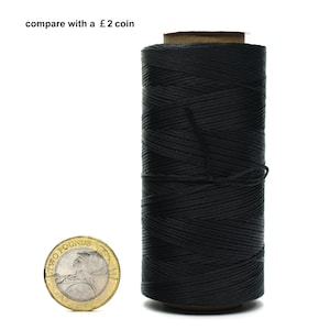 Op de afbeelding: Een spoel met zwarte gewaxt draad voor lederbewerking, naast een munt van twee pond voor een groottevergelijking. De draad is strak op de spoel gewikkeld.