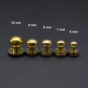 Op de afbeelding: Vijf messingkleurige koepelvormige knoppen in verschillende maten, variërend van 6 mm tot 10 mm in diameter. De knoppen zijn gerangschikt op grootte, met de grootste knop links en de kleinste knop rechts.