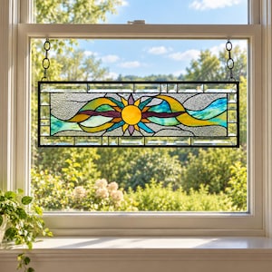 May include: A rectangular stained glass window hanging featuring a central yellow sun motif surrounded by flowing abstract shapes in shades of blue, teal, purple, and yellow. The panel is framed by clear beveled glass and black metal cames.