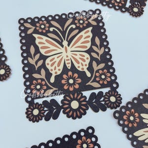May include: Close-up of several dark brown, square-shaped paper cutouts with a scalloped edge. Each cutout features a butterfly and floral design in shades of tan and brown. The text "Crafts by Betty" is visible.