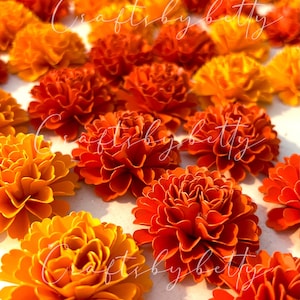 May include: An overhead shot showcases a collection of vibrant, orange and yellow paper flowers. The flowers are arranged closely together, creating a dense, textured display. The text "craftsbybetty" is written across the image in a cursive font.