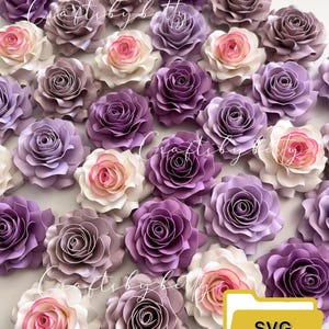 Puede incluir: Una colección de 20 flores de papel en tonos de morado, rosa y blanco. Las flores están superpuestas y tienen un aspecto realista. La imagen incluye el texto ".SVG .STUDIO" en una carpeta amarilla.