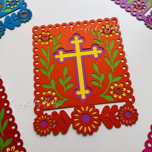 May include: A vibrant, layered paper cutout featuring a yellow and purple cross on a red background, framed by green leaves and yellow flowers. The design includes the text "CraftsbyBetty" and is surrounded by decorative floral cutouts in red, purple, and blue.