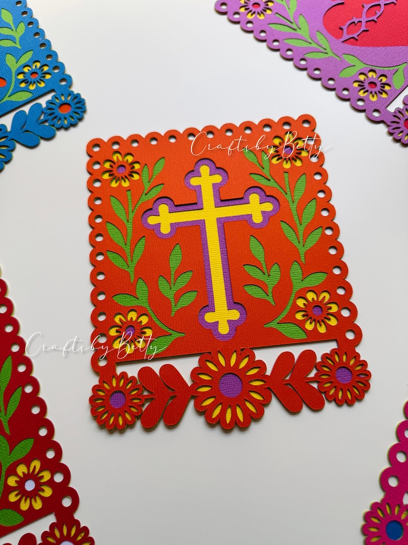 May include: A vibrant, layered paper cutout featuring a yellow and purple cross on a red background, framed by green leaves and yellow flowers. The design includes the text "CraftsbyBetty" and is surrounded by decorative floral cutouts in red, purple, and blue.