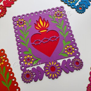 May include: Close-up of colorful paper cutouts. A purple square with a red heart and yellow flames is surrounded by flowers and green leaves. The text "Crafty by Betty" is visible. Other cutouts in red and blue are also visible.