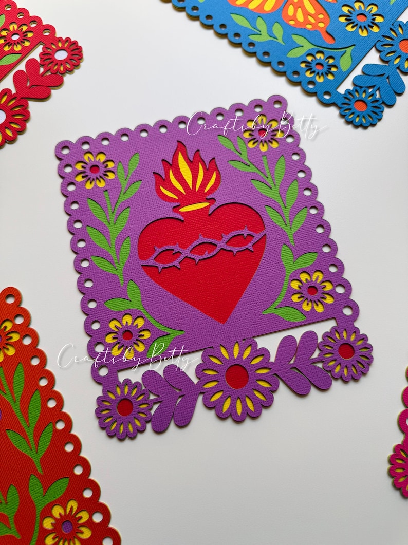 May include: Close-up of colorful paper cutouts. A purple square with a red heart and yellow flames is surrounded by flowers and green leaves. The text "Crafty by Betty" is visible. Other cutouts in red and blue are also visible.