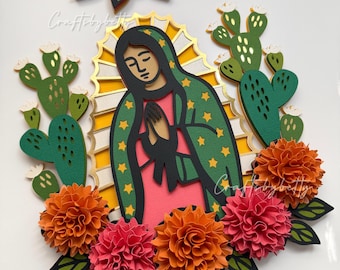 May include: Layered paper art depicting the Virgin Mary, surrounded by orange and pink paper flowers, green cacti, and a gold halo. The Virgin Mary is wearing a green robe with gold stars and a pink dress. The artwork is set against a white background.