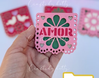 May include: Pink paper cut-out with a green flower design and the word "AMOR" in red. The cut-out is part of a set of paper cut-outs for a Mexican fiesta or celebration. The file is available in SVG and Studio formats.