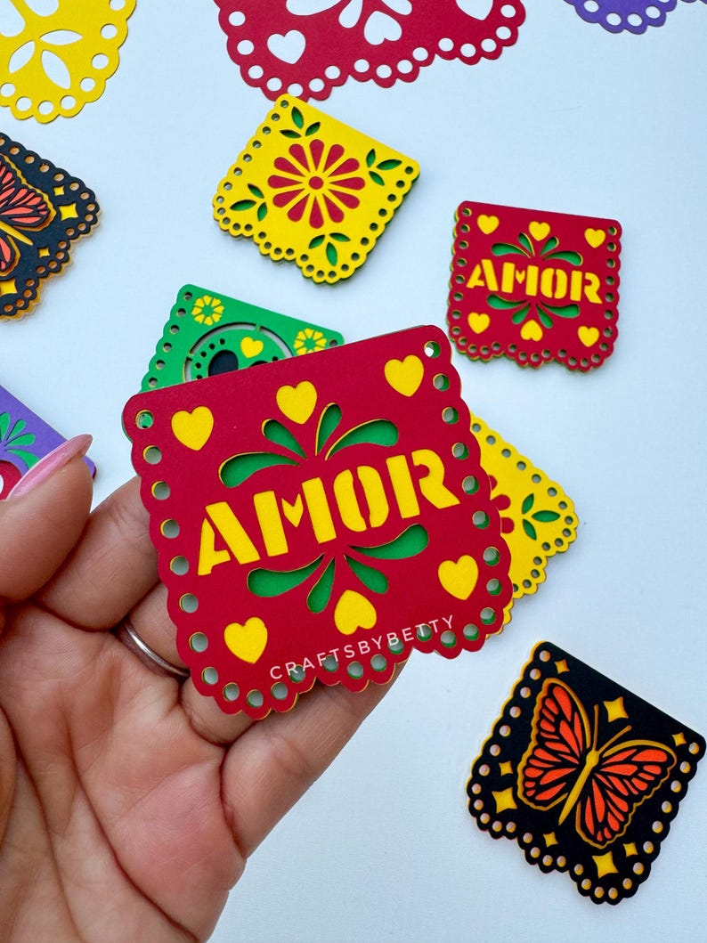 May include: A set of colorful paper cutouts with a butterfly, flowers, and the word "AMOR" in yellow letters on a red background. The cutouts are decorated with hearts and a scalloped edge.