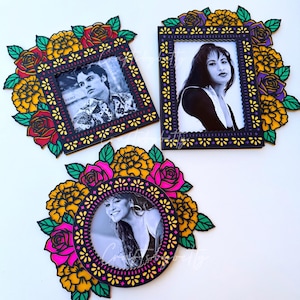 Puede incluir: Tres marcos de fotos decorativos con diseños negros y florales. Cada marco contiene una foto en blanco y negro de una persona. Los marcos están adornados con flores coloridas en tonos amarillos, rosas y rojos.