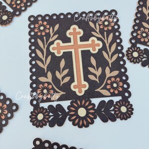 May include: Brown and beige die-cut paper crafts with a cross design. The cross is centered on a dark brown square, surrounded by floral and leaf accents. The text "Craftsbybetty" is visible. Additional floral cutouts are scattered around.