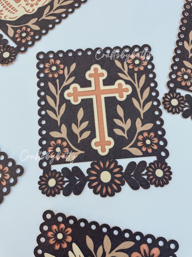 May include: Brown and beige die-cut paper crafts with a cross design. The cross is centered on a dark brown square, surrounded by floral and leaf accents. The text "Craftsbybetty" is visible. Additional floral cutouts are scattered around.