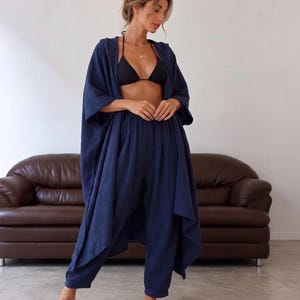May include: A dark blue two-piece set consisting of a loose-fitting, hooded, open-front long-sleeve cover-up and matching high-waisted, tapered-leg pants. The fabric has a visible crinkled texture throughout the entire garment.