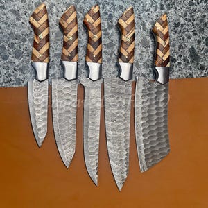May include: A set of six kitchen knives with patterned steel blades and wooden handles. The handles feature a herringbone design in light and dark wood, secured with small metal rivets. The blades have a textured surface.