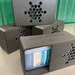 May include: A stack of dark grey cooler units. Each unit features a honeycomb vent and a sliding door. One unit is open, displaying a blue ice pack. The text "TAYTAY'S COOLER UNIT" is printed on one of the units.